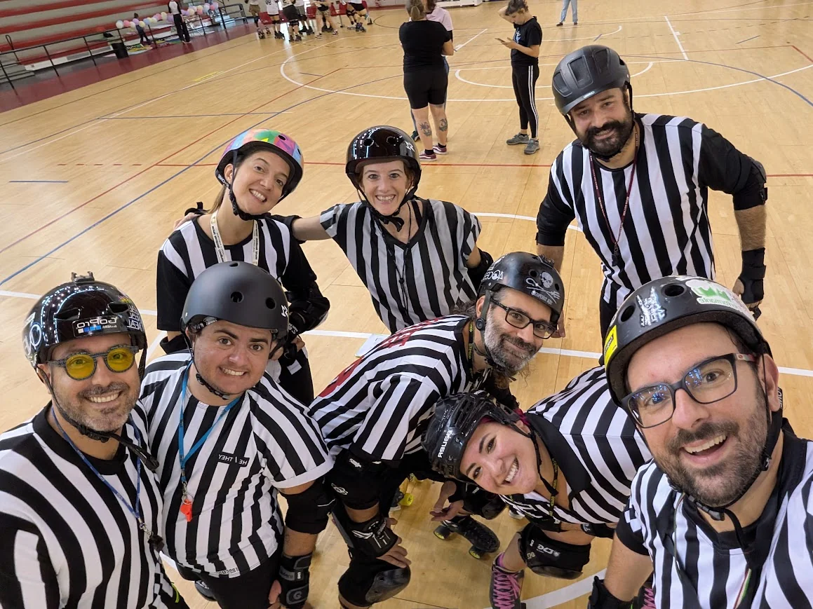 Foto di gruppo sul campo di roller derby, con caschi, pattini e maglie da arbitro