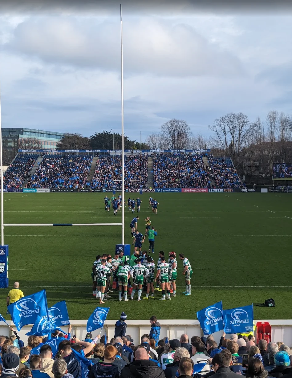 Una squadra di rugby riunita in cerchio sul campo, davanti alle tribune